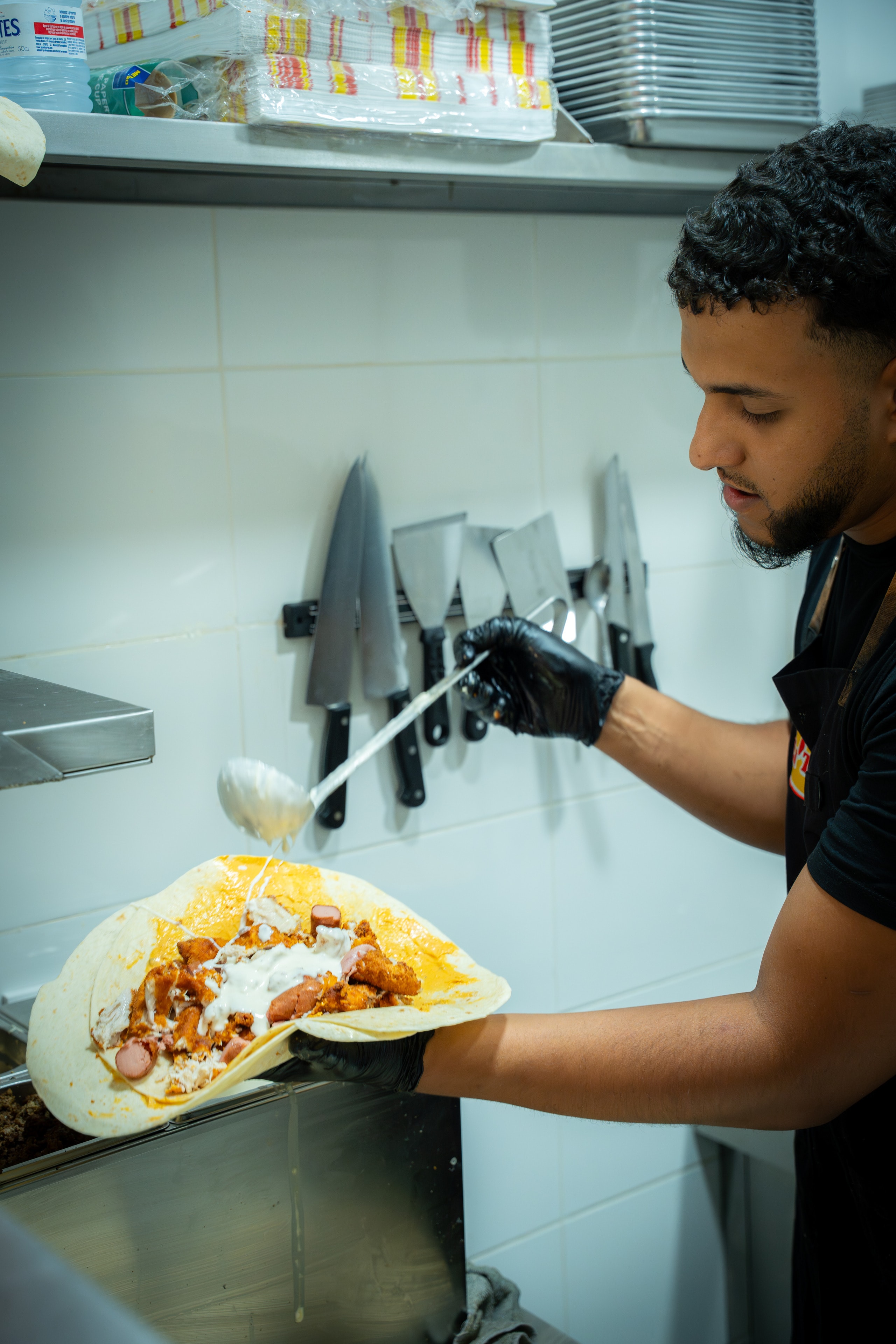 Un cocinero de LiTaco con guantes negros echa salsa sobre un taco abierto recién montado